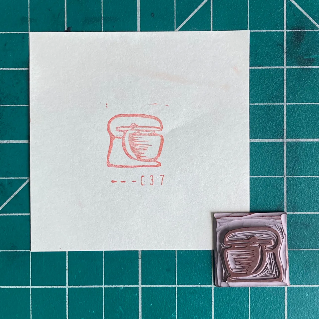 The composition features a white paper on a teal grid displaying a red pencil drawing of a pot and the number 037, alongside a matching reddish-brown molded object.
