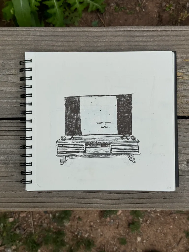 A black and white sketch of a rectangular cabinet with solid black sides and three drawers, drawn on white paper and placed on an open spiral sketchbook on a wooden surface.