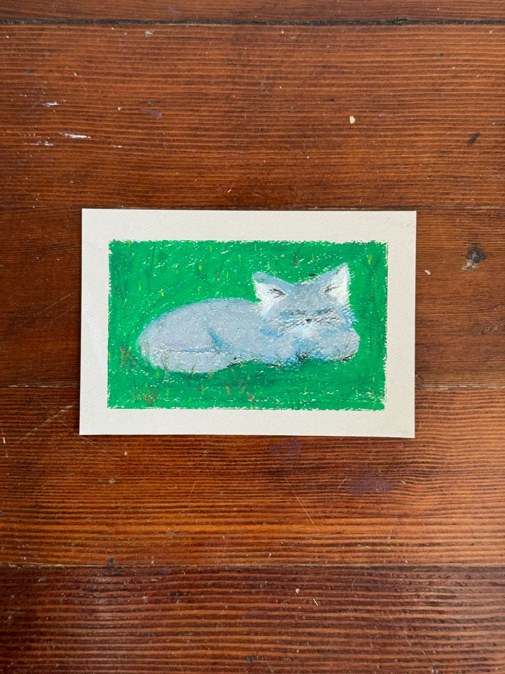 A stylized light blue animal rests on a solid green painted background, framed by a cream border.