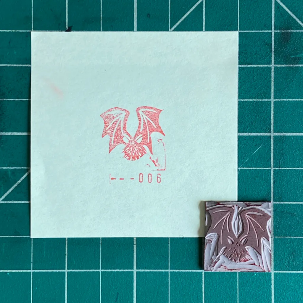 A white square features a red drawing of two stylized wings and the number 006, positioned next to a small square object displaying symmetrical reddish-brown and white floral patterns on a teal grid background.