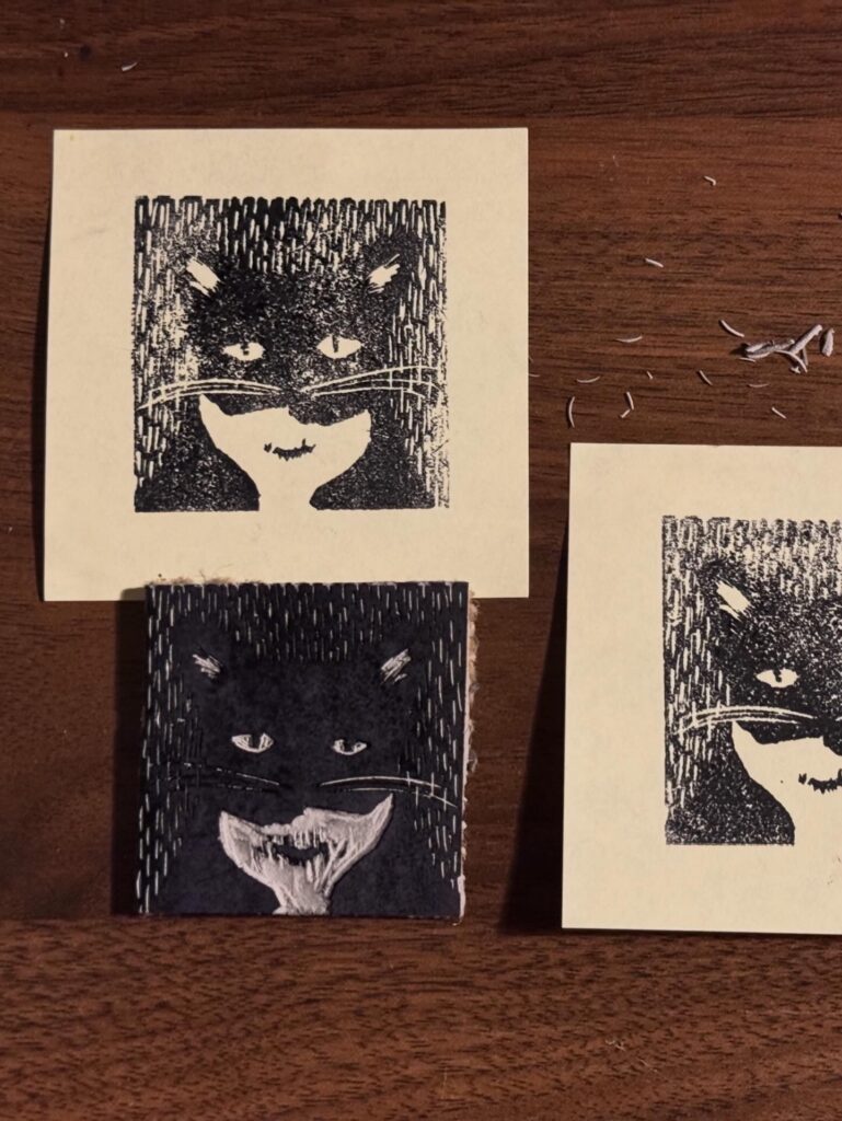 A print of a cat on a sticky note next to the stamp that was used to make it.