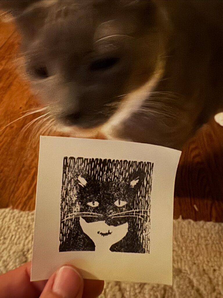 A cat smelling a print of a cat on a sticky note.