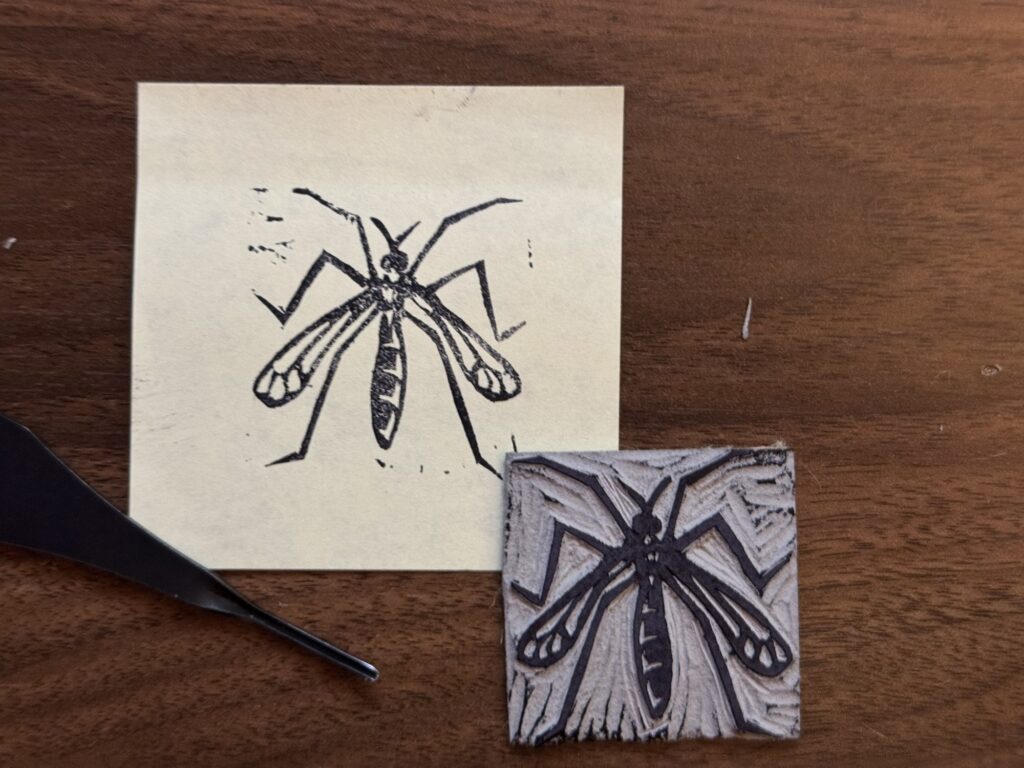 A print of a crane fly next to its stamp and carving tool.